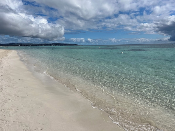 A beach with clear turquoise water, a sandy shore, and a distant island.
