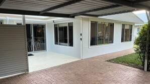 A covered patio area with a brick floor, large windows, and a small lawn.