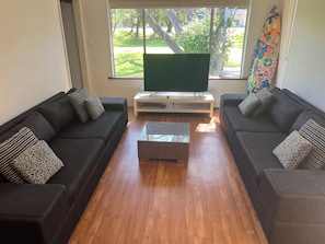 A living room with two dark sofas, a glass coffee table, and a flat-screen TV on a stand.