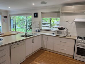A modern kitchen with white cabinets, a dishwasher, a microwave, a stove, and a window with a view of greenery.