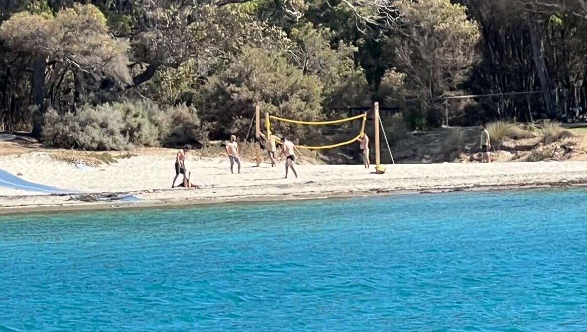 Een strandvolleybalwedstrijd op een zandstrand met een heldere blauwe zee op de voorgrond.
