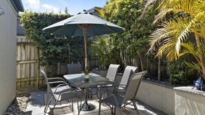 An outdoor patio with a table and chairs, a large umbrella, and a wooden fence. - Husky House by Experience Jervis Bay (Huskisson)