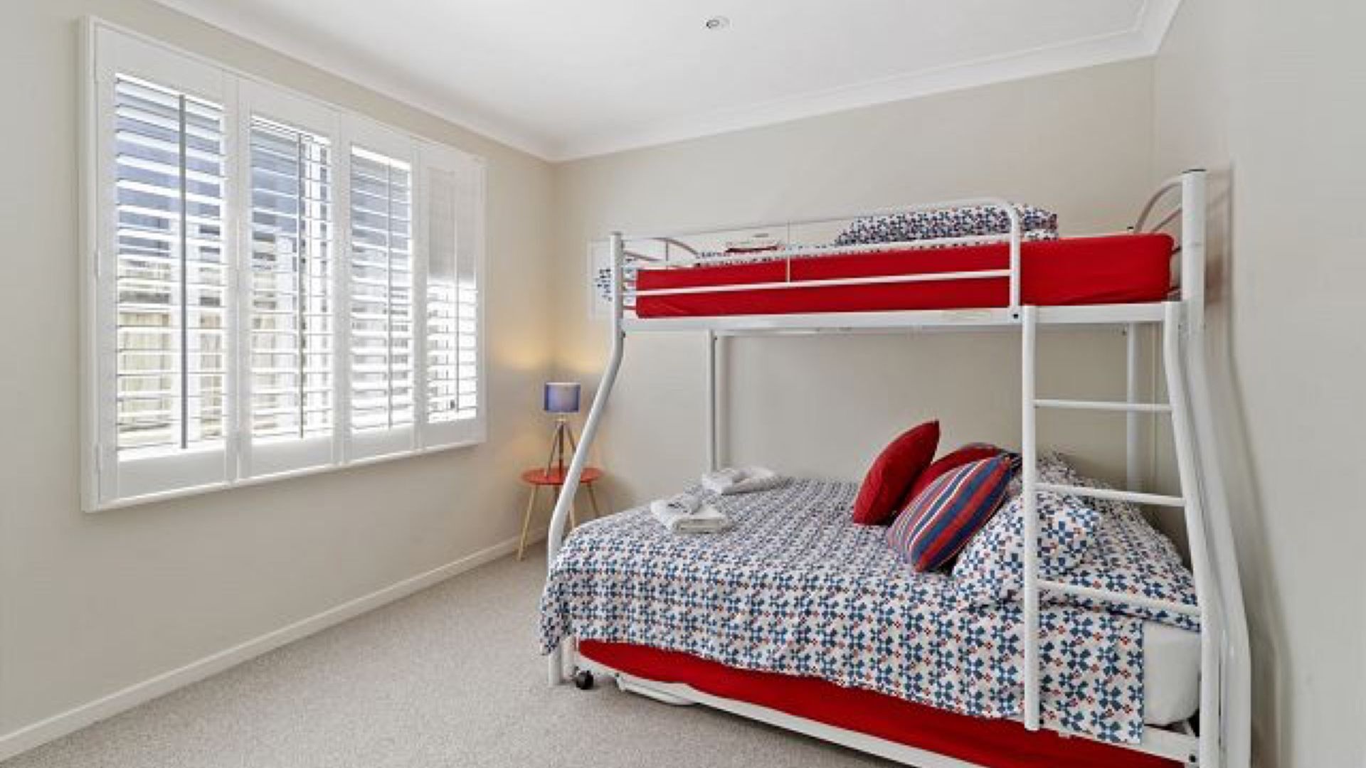 Een slaapkamer met een stapelbed, een raam, een lamp en een klein tafeltje.