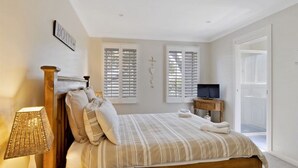 A bedroom with a bed, a bedside table with a lamp, a TV, and a sliding door to a balcony. - Husky House by Experience Jervis Bay (Huskisson)