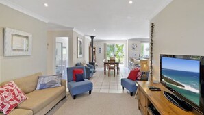 A spacious living room with a large TV, comfortable seating, and a view of the ocean. - Husky House by Experience Jervis Bay (Huskisson)