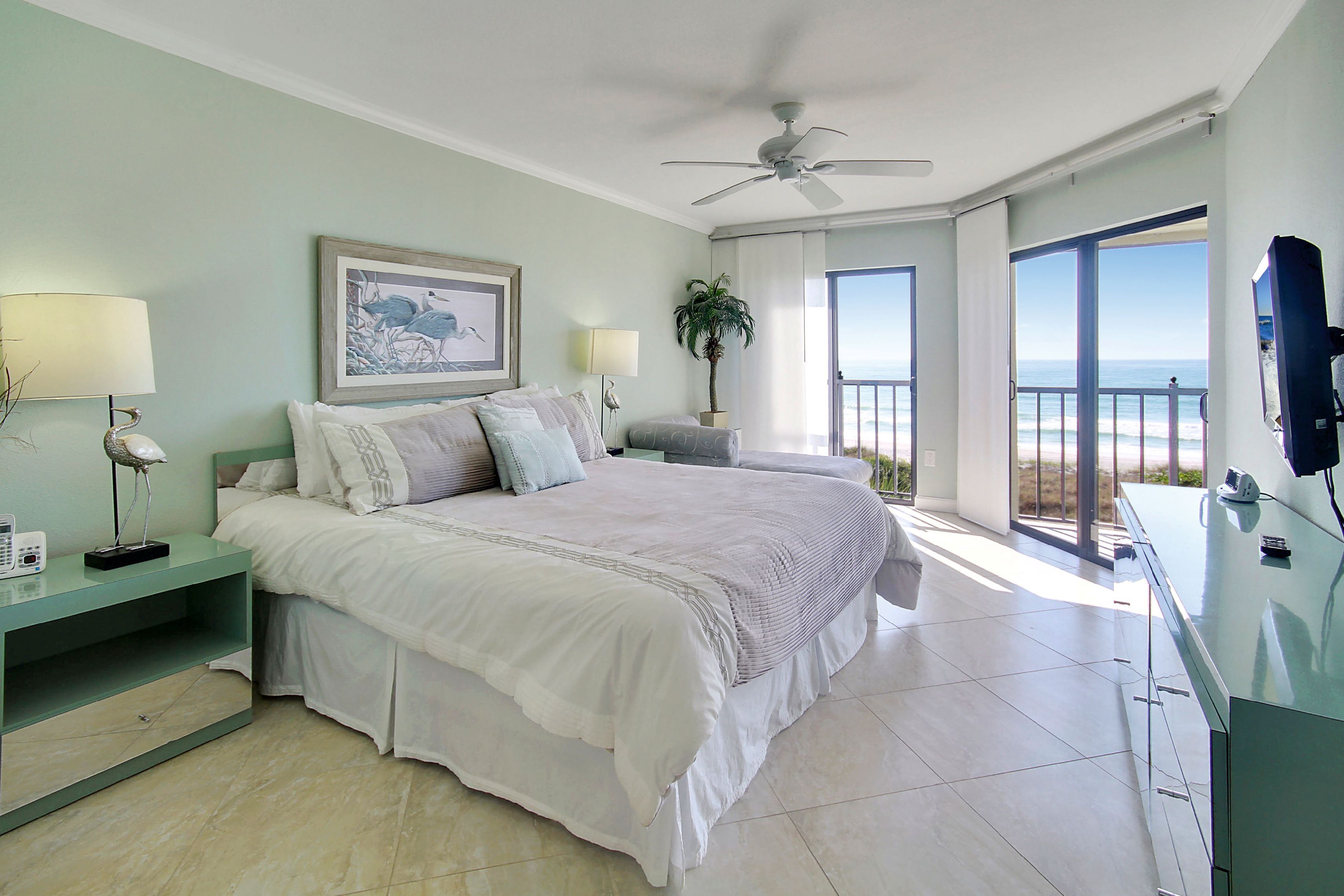 Ruime slaapkamer met een groot bed, een plafondventilator en een balkon met uitzicht op de oceaan.