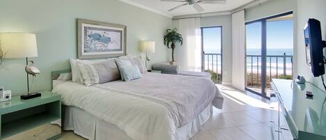 Ruime slaapkamer met een groot bed, een plafondventilator en een balkon met uitzicht op de oceaan.
