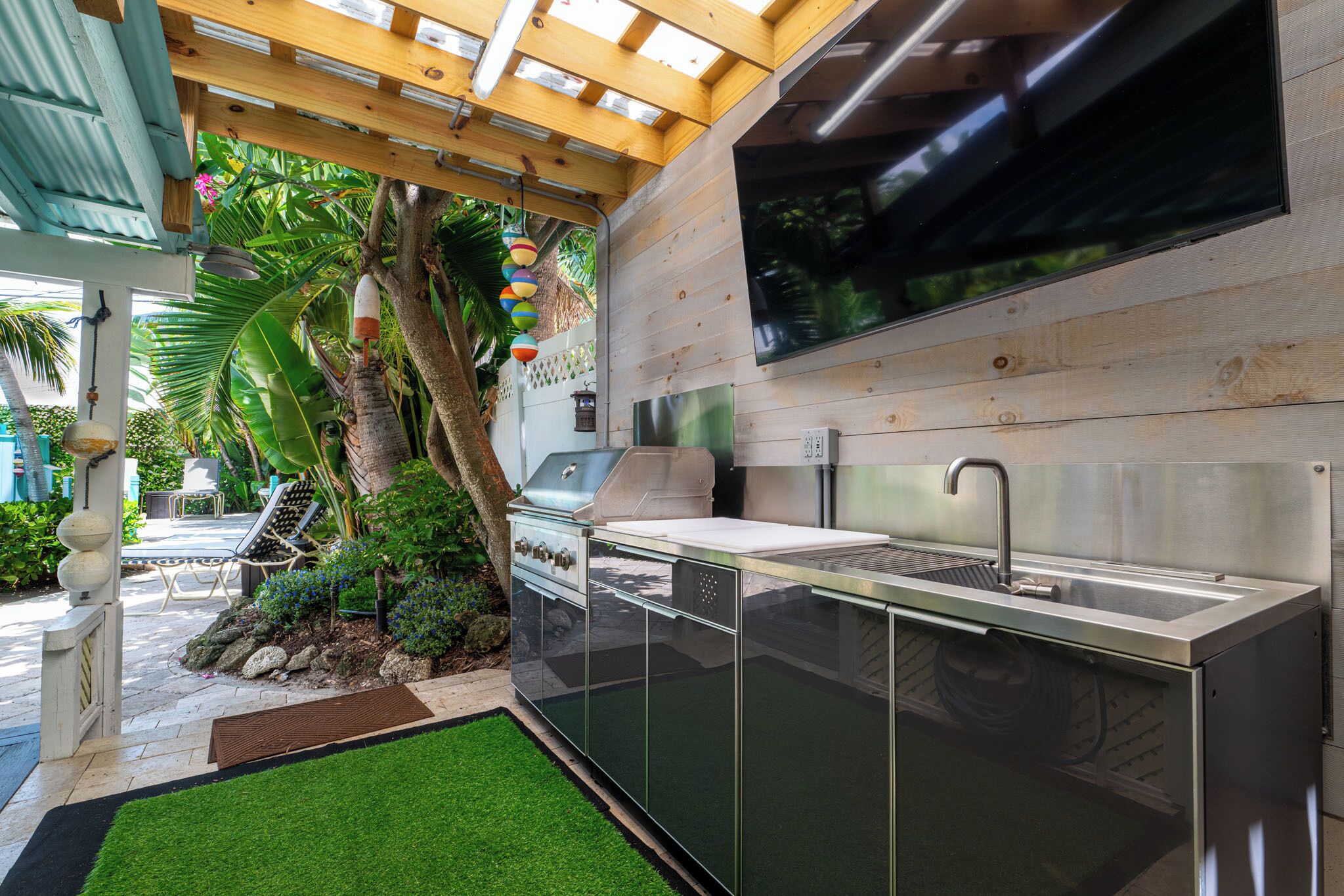 An outdoor kitchen with a built-in grill, a sink, and a stainless steel countertop.
