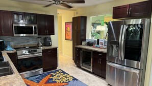A modern kitchen with dark wooden cabinets, stainless steel appliances, and a colorful rug. - Resort Style Home Steps To Beach/ Heated Pool/ Game Room/ Top Rated! (Singer Island)