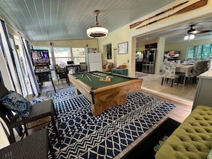 A pool table in a room with a patterned rug, a dining area with a table and chairs, and a kitchen area with a refrigerator and stove. - Resort Style Home Steps To Beach/ Heated Pool/ Game Room/ Top Rated! (Singer Island)