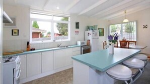 A modern kitchen with white cabinets, a central island with bar stools, a refrigerator, and a window providing natural light.