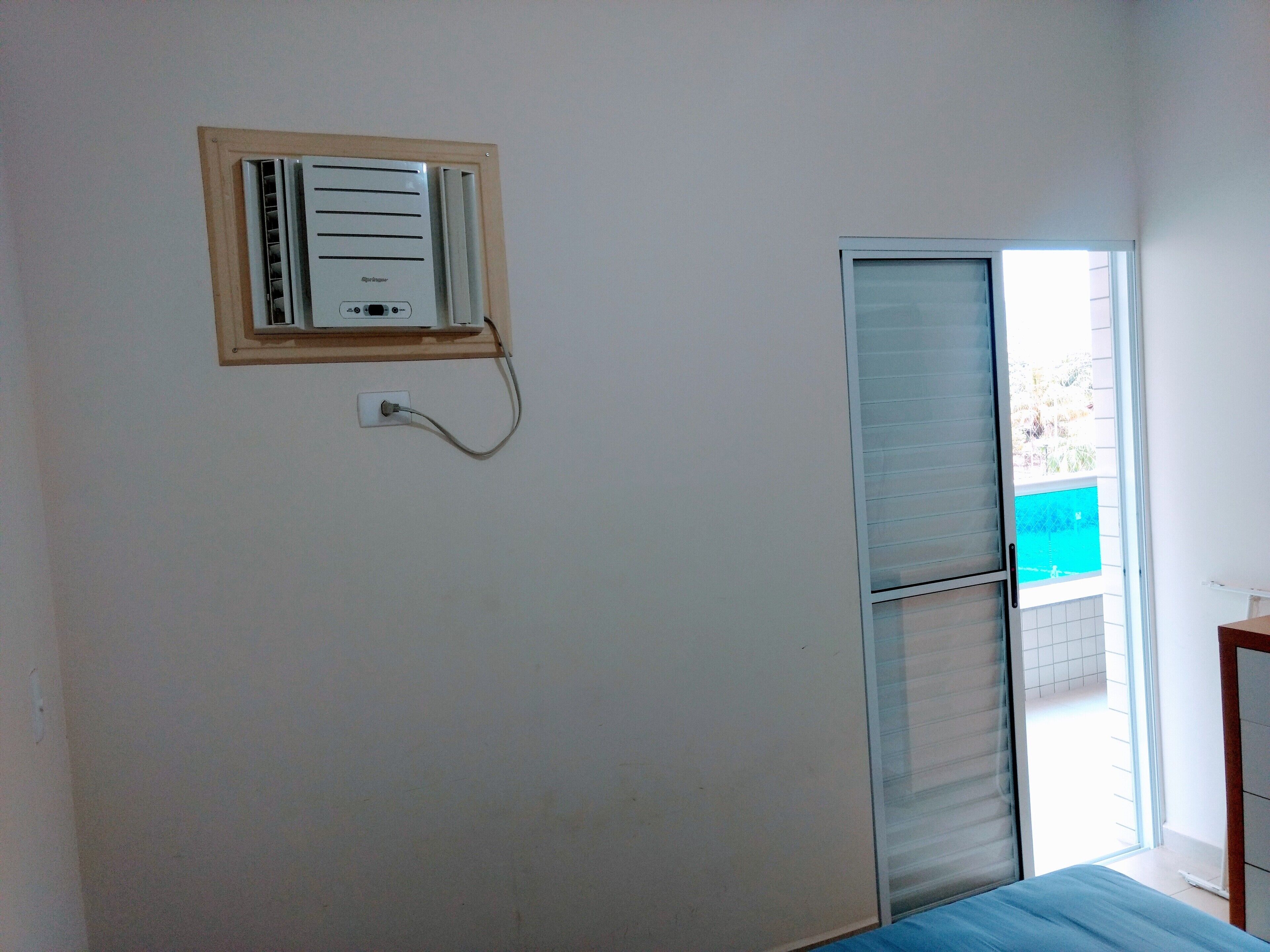A room with a window, a wall-mounted air conditioning unit, and a door leading to an outdoor area.