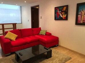 Un sofá rojo con un cojín amarillo, una mesa de centro negra y dos cuadros abstractos en la pared.