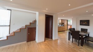 Un vaste espace de vie agrémenté d’un escalier en bois, d’une table à manger avec des chaises, et d’une cuisine en arrière-plan.