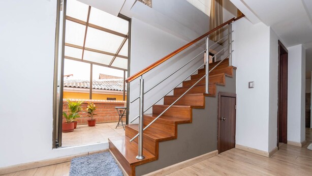 Un intérieur moderne avec un escalier en bois, une vue sur l’extérieur et un petit balcon agrémenté de plantes en pot.