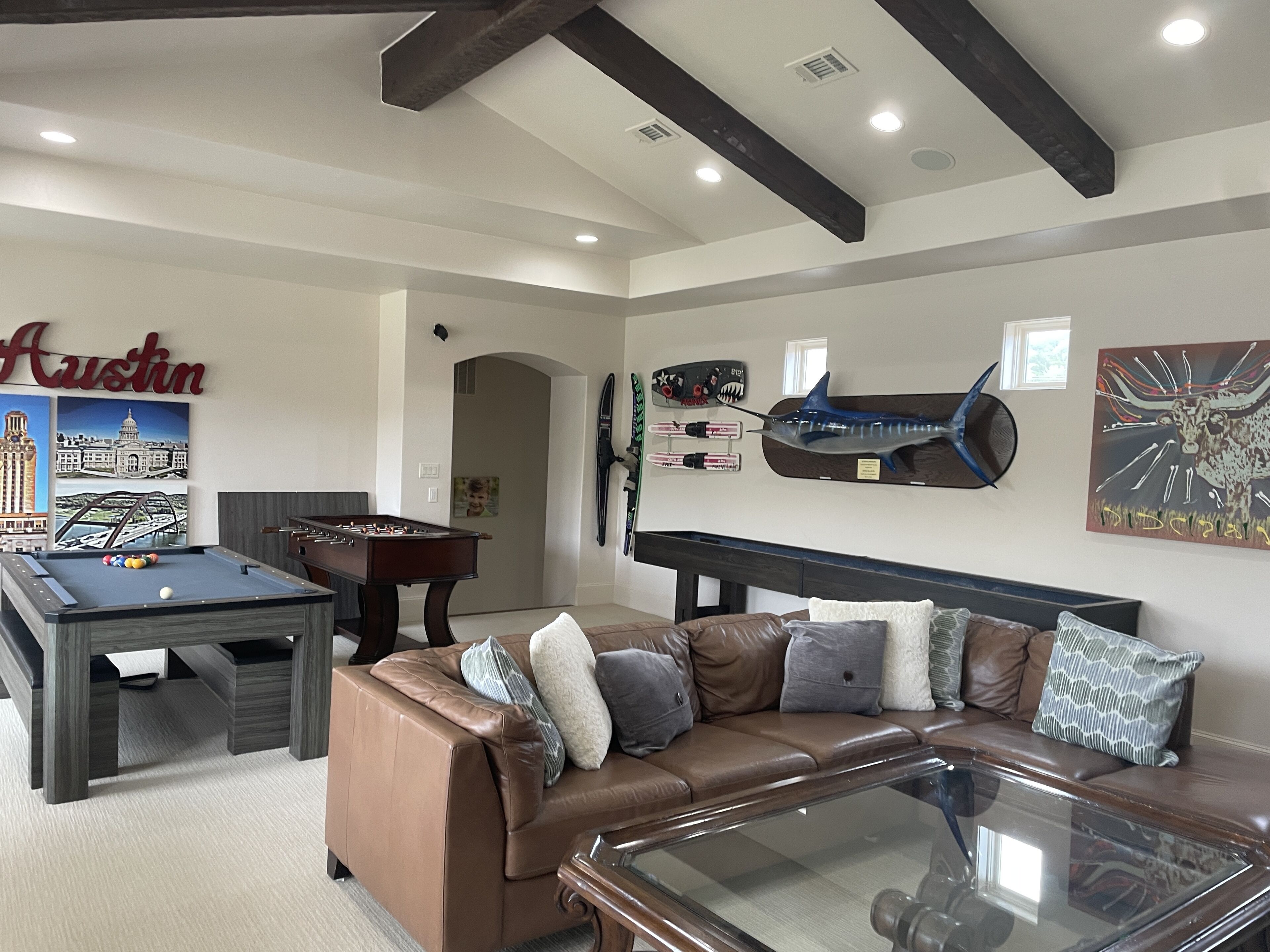 A living room with a foosball table, a pool table, a brown leather couch, and a glass coffee table.