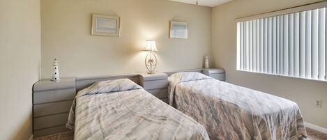Une chambre avec deux lits, un ventilateur de plafond, une table de chevet avec une lampe et une fenêtre avec des stores.