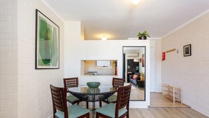 A modern apartment with a dining area featuring a round table and four chairs, a kitchen with a built-in oven, and a living area with a sofa and a TV. - Stay OK Central Fremantle (Fremantle)