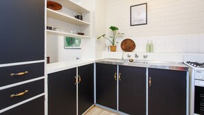 A modern kitchen with black cabinets, white countertops, and a gas stove. There is a framed picture on the wall and a potted plant on the counter. - Stay OK Central Fremantle (Fremantle)