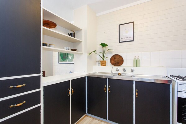 A modern kitchen with black cabinets, white countertops, and a gas stove. There is a framed picture on the wall and a potted plant on the counter. - Stay OK Central Fremantle (Fremantle)