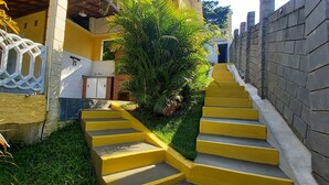 A set of yellow stairs leading up to a building with a white door and a small garden area with green plants. - Country house in Igaratá, standard model, with cable TV, internet, swimming pool, and gourmet area. (IGARATA)