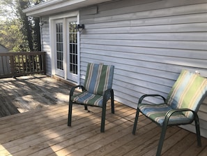 Eine Holzterrasse mit zwei gestreiften Stühlen und einer weißen Tür.