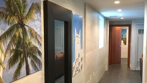 A hallway with a modern design, featuring a large framed picture of a palm tree, a framed picture of a building, and a door at the end. - Miami Beach 3BD Luxury Condo Suite (201) (Miami Beach)