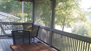 Eine Holzterrasse mit Tisch und Stühlen, einem Deckenventilator und Blick auf Bäume durch das Geländer.
