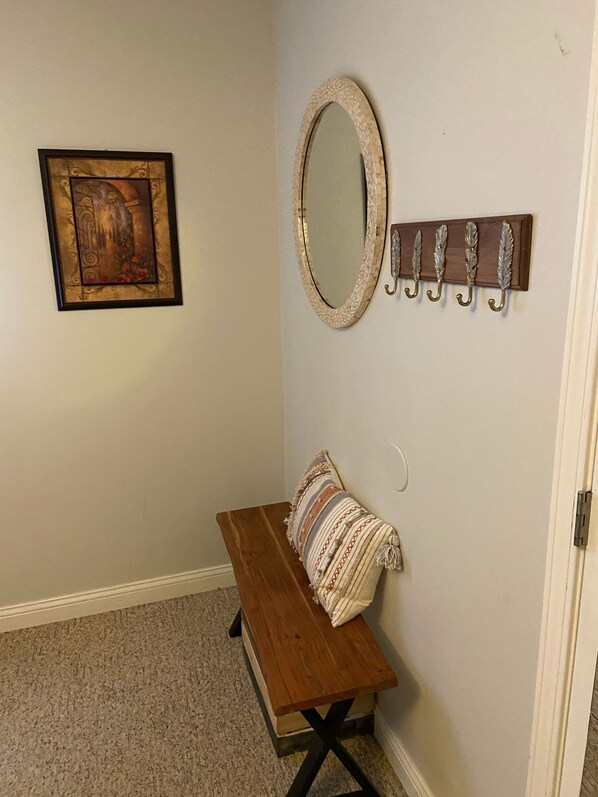 A hallway with a wooden bench, a mirror, a framed picture, and a coat rack.