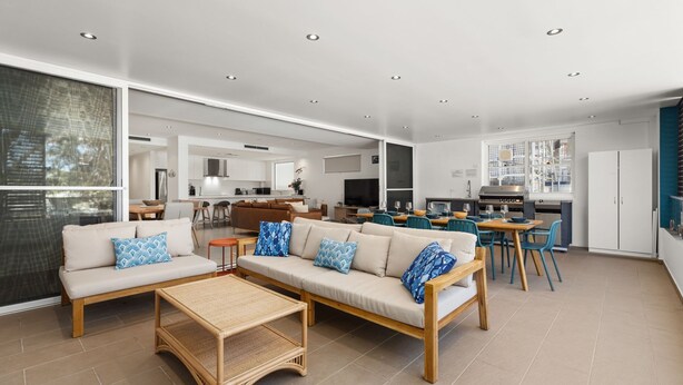 A spacious living area with a sofa set, a dining table, and a kitchen in the background. - Salty Steves by Experience Jervis Bay (Huskisson)