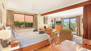 A bedroom with a bed, a desk, a chair, a TV, and a balcony with a view of greenery. - Alva Lee by Experience Jervis Bay (Vincentia)