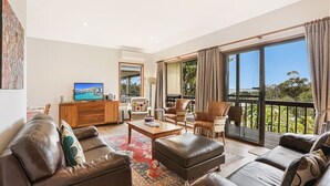 A spacious living room with a large flat-screen TV, leather sofas, a coffee table, and a balcony with a view of the sea. - Alva Lee by Experience Jervis Bay (Vincentia)
