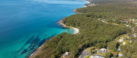 An aerial view of Jervis Bay with a coastal road, residential houses, and a beach.