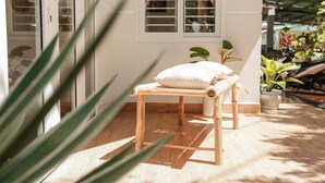 Een houten bank met kussen en een bloempot in een goed verlichte kamer met raam en deur.