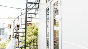 Een smal balkon met een spiraaltrap, glazen deuren en uitzicht op groen.