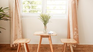Een kamer met een houten tafel, twee bijpassende krukken, een vaas met groen en een raam met gordijnen.
