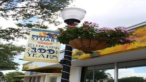 A building with a sign celebrating 100 years, a street lamp, and a hanging flower basket. - Stuart Cottage II Pet Friendly, Remodeled, close to beach and quaint downtown (Stuart)