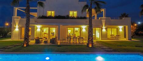 A modern two-story house with a swimming pool, outdoor seating area, and palm trees.