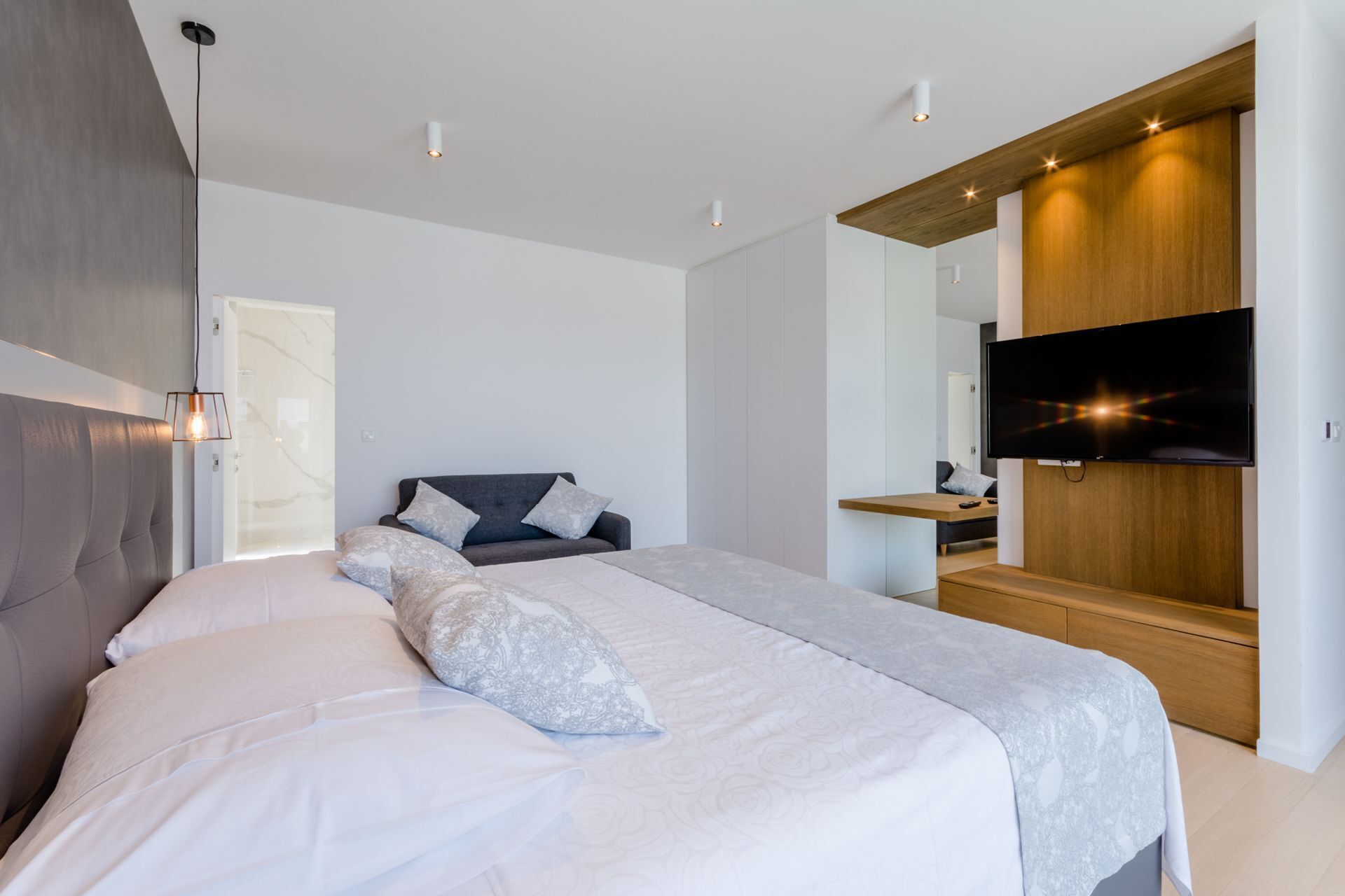 A modern bedroom with a large bed, a TV mounted on a wooden panel, and a built-in wardrobe.