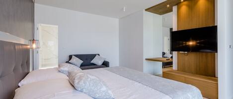 A modern bedroom with a large bed, a TV mounted on a wooden panel, and a built-in wardrobe.
