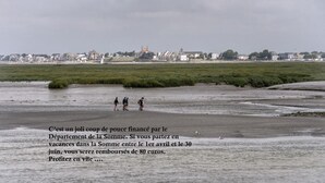 Ein Strand mit Spaziergängern, eine ferne Stadt und ein Gewässer.