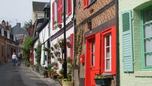 Eine enge Straße gesäumt von traditionellen europäischen Gebäuden, manche mit roten Fensterläden und Blumenkästen.