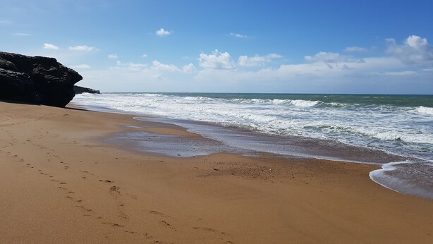 Une plage avec un promontoire rocheux et des vagues qui déferlent sur le rivage.