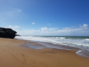 Una playa con un promontorio rocoso y olas rompiendo en la orilla.