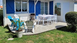 Une maison avec un toit en tuiles, des volets bleus et une terrasse aménagée avec du mobilier d’extérieur.
