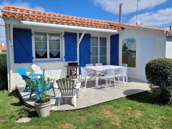 Una casa con techo de tejas, contraventanas azules y un patio con mobiliario exterior.