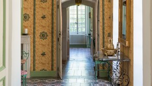 Un corridoio con carta da parati decorata, pavimento piastrellato e uno specchio con cornice verde.
