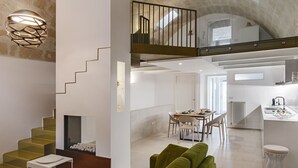 A modern interior with a staircase, green sofa, dining area, kitchen, and a balcony with a railing.