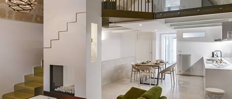 A modern interior with a staircase, green sofa, dining area, kitchen, and a balcony with a railing.