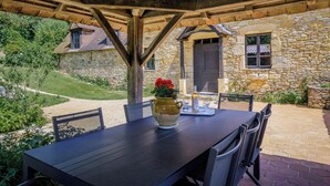 Een terras buiten met een stenen muur, houten balken en een tafel met stoelen.
